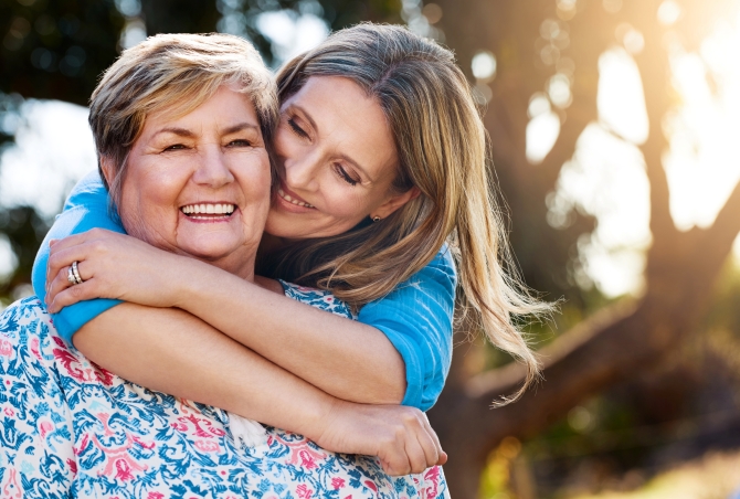Middle-aged daughter hugging her aging parent from behind